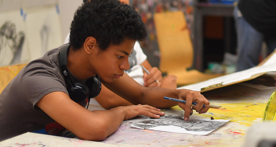 young artist seated, working on a graphite drawing